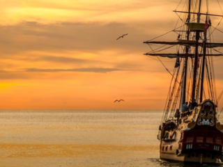 Old sail boat on the water, sailing into the sunset.