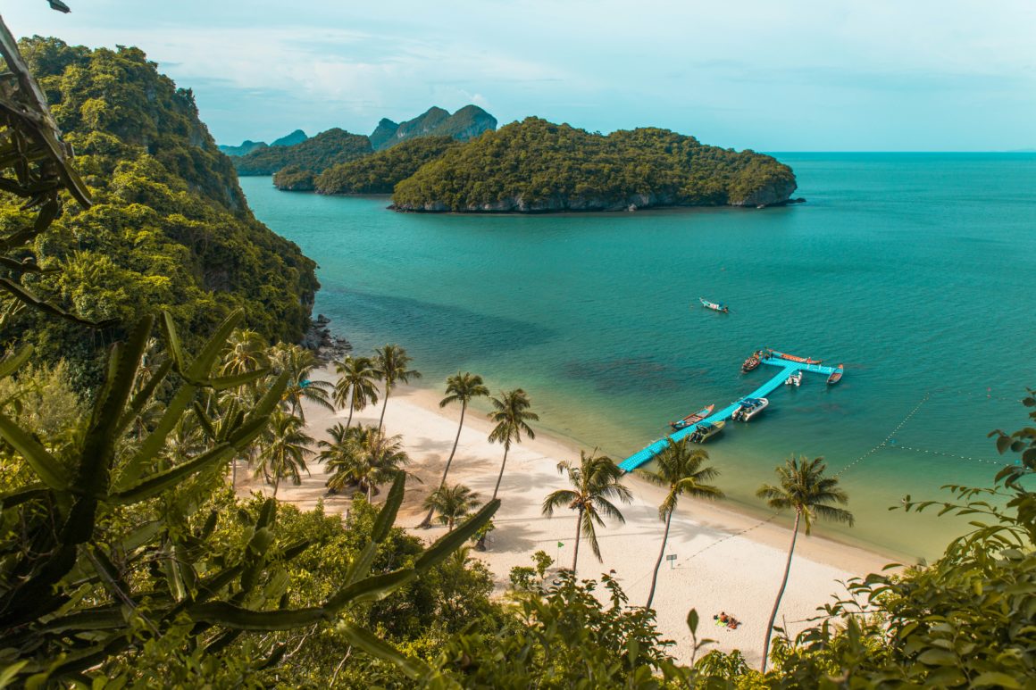 Aerial view of a palm-fringed beach with boats moored to a floating pier in Thailand