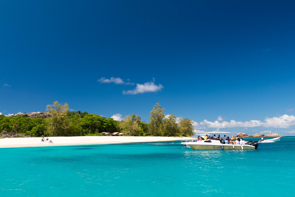Speedboats anchored off a white-sand beach in the Seychelles with turquoise water.