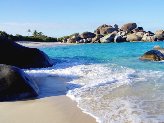 Small sandy beach with turquoise waves washing over rocks and large boulders in the Caribbean.