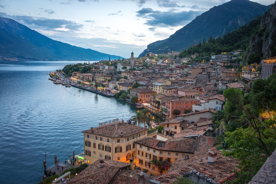 Lakeside Italian town at dusk with tiled rooftops overlooking a calm mountain lake.