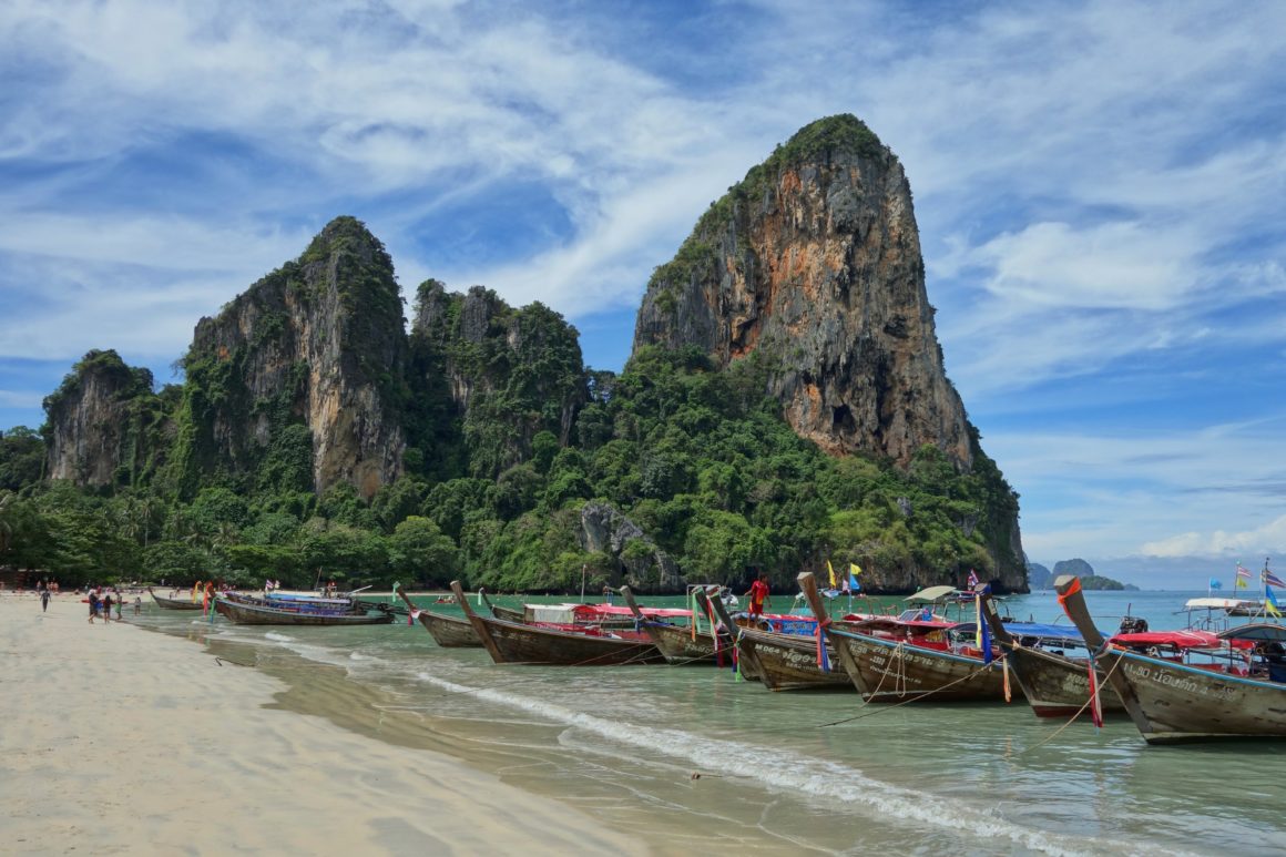 Traditional long-tail boats moored on a sandy beach near limestone cliffs in Thailand