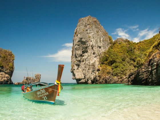 Long-tail boat anchored in shallow turquoise water by steep cliffs in Thailand