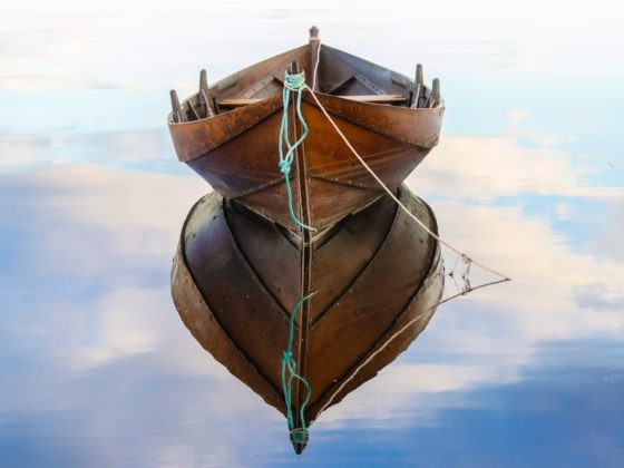 Front view of a wooden rowboat floating on calm water, emphasizing its width or beam through a perfect reflection.