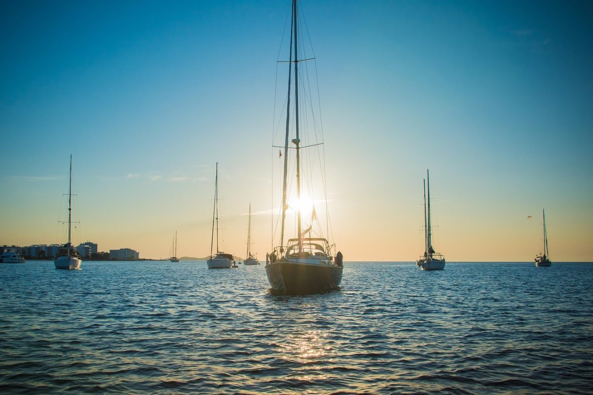 Sailboats anchored off Ibiza at sunset with the sun behind a mast.
