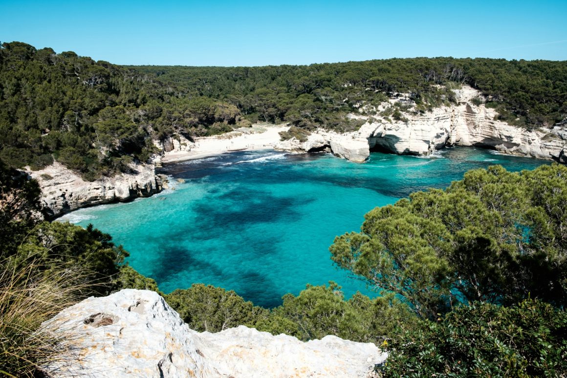 Turquoise cove surrounded by pine forest and white cliffs in Menorca.