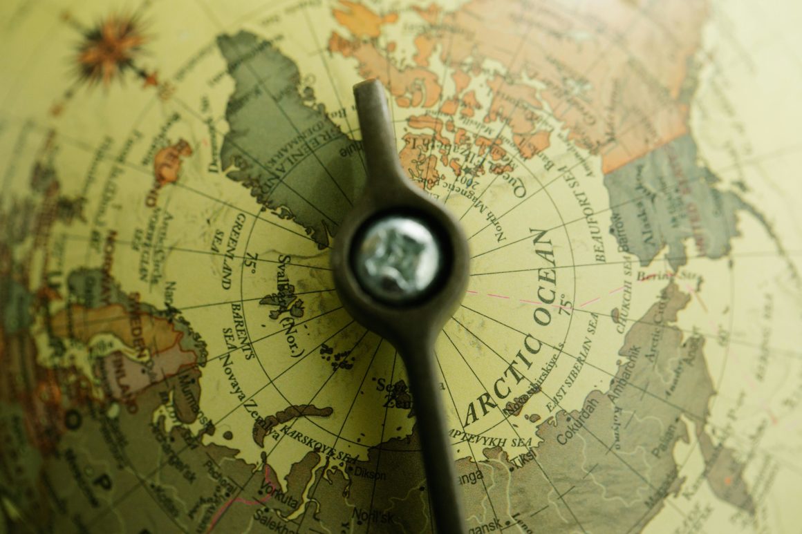Close-up of a world globe showing latitude and longitude lines near the Arctic Ocean, with a central position marker.
