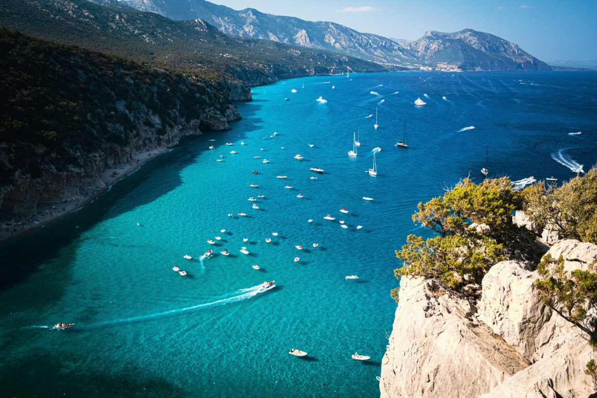 Boats sailing near the rugged cliffs and turquoise bays of Sardinia.