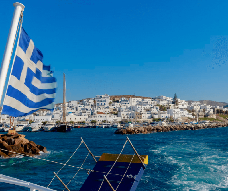 Un barco con la bandera de Grecia y el mar azul en el fondo 