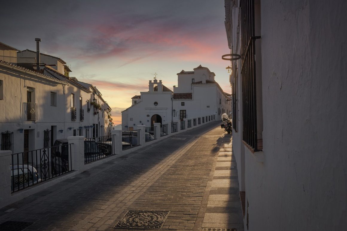 Imagen que muestra una calle típica de Andalucía, con sus casas blancas y el atardecer de fondo. 