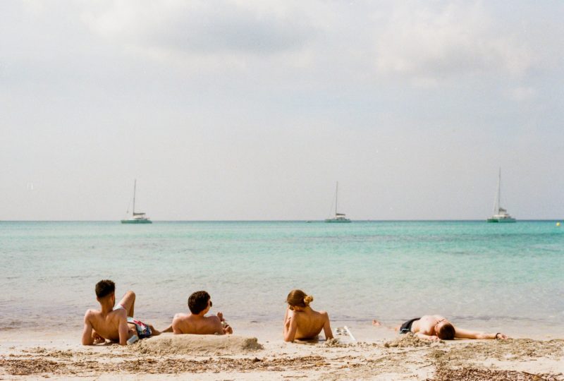 Amigos disfrutando de un día de sol y playa, tumbados en la arena. 