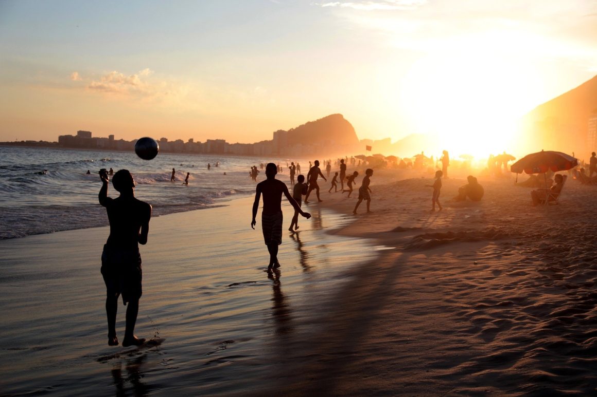 Atardecer en la playa de Copacabana. Personas juegan en la playa y se bañan en el mar.