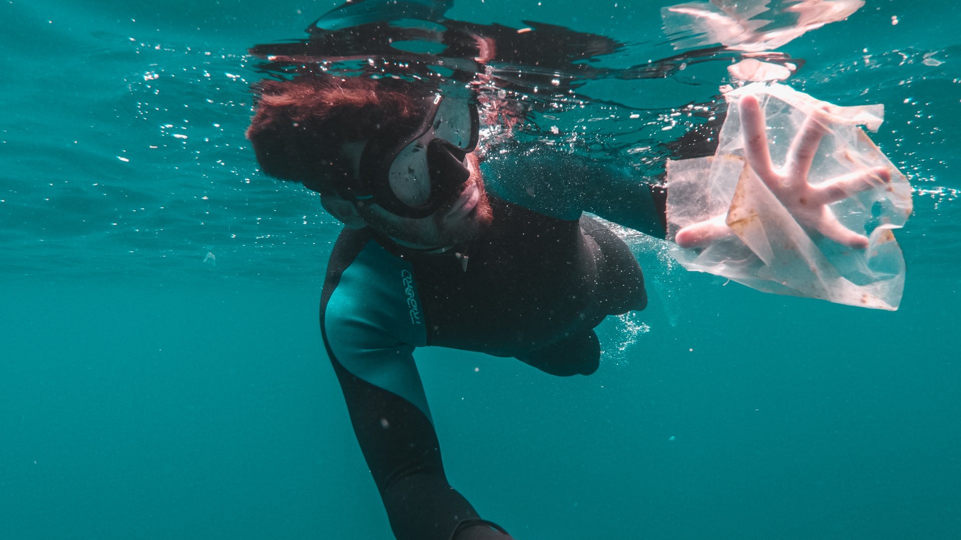 Hombre recogiendo plásticos del mar para evitar la contaminación marina