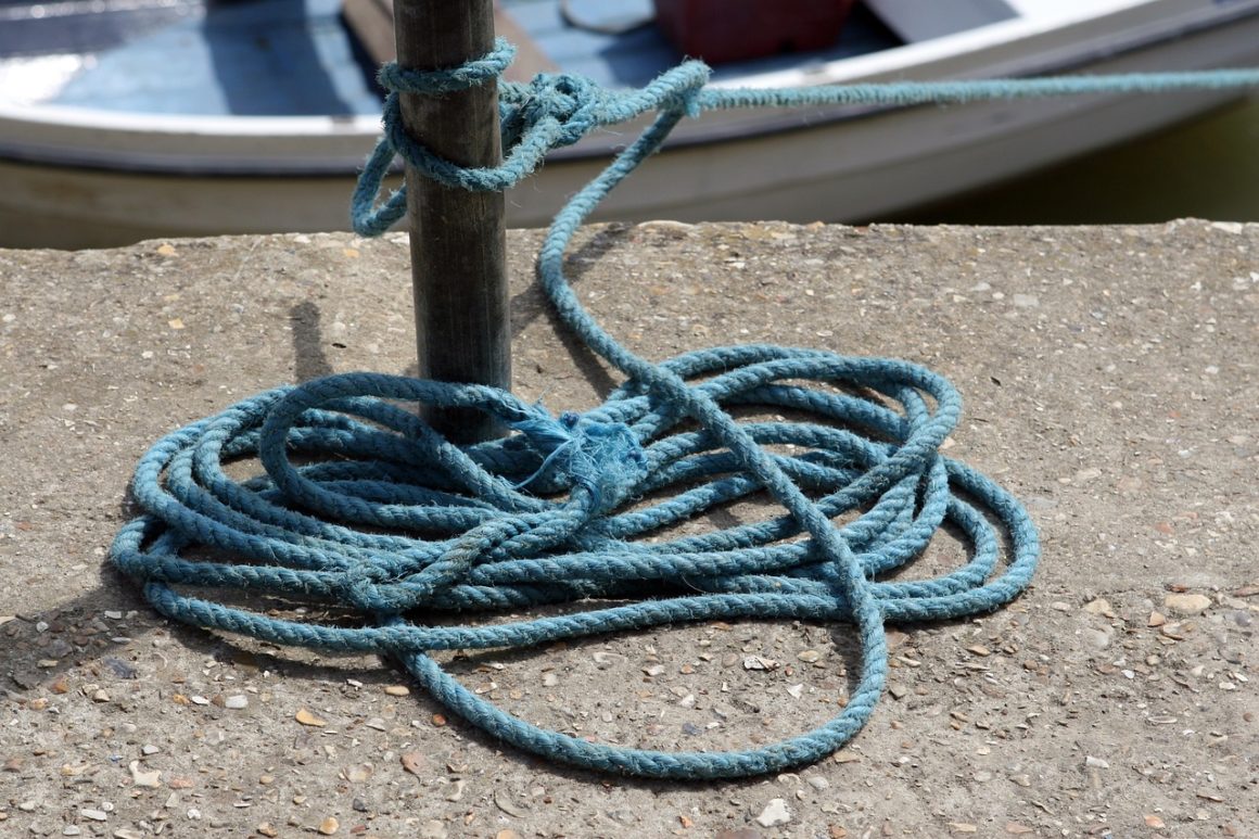 Imagen que muestra una cuerda de color azul que está atada con un nudo en un palo del puerto.