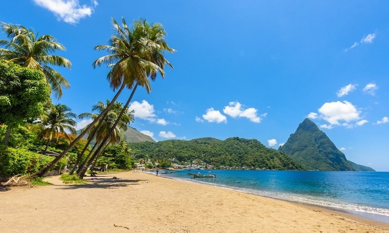 spiaggia Santa Lucia con palme, mare azzurro e montagne all'orizzonte