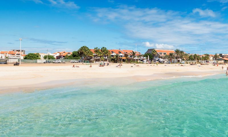 Vistua sulla spiaggia bianca e le acque cristtalline di Capo Verde, con case e palme sullo sfondo, per la pasqua al mare