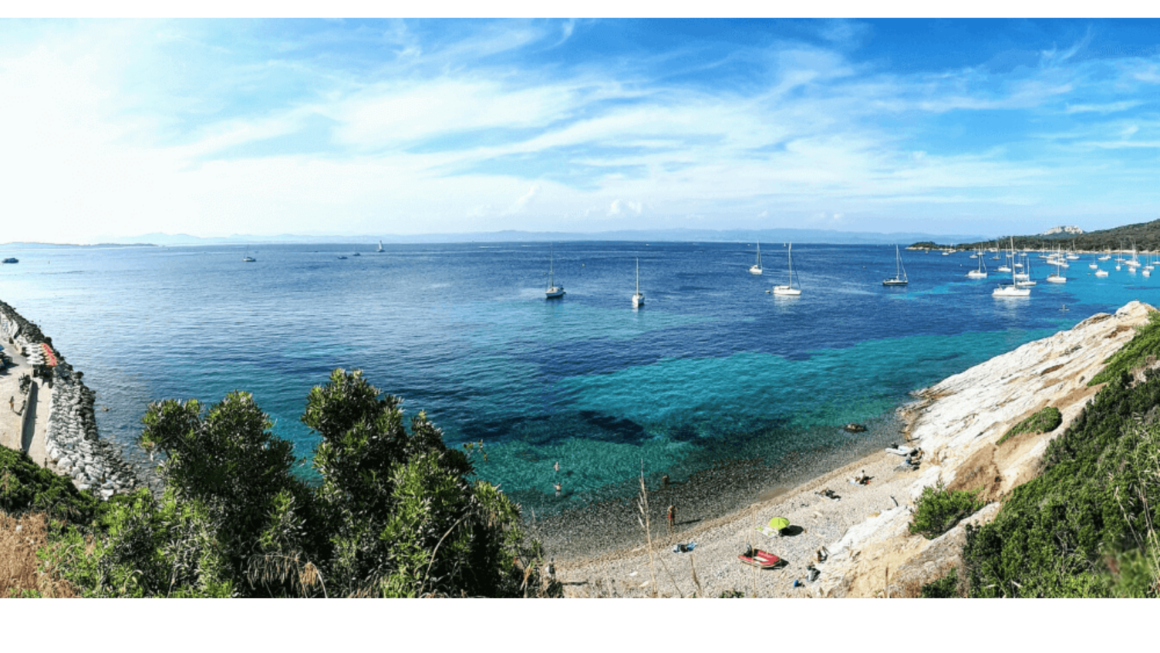 Spiaggia di ciottoli e mare turchese nel sud della Francia, con numerose barche a vela all’ancora al largo.