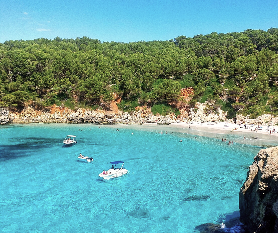 Baia turchese di Cala Escorxada con barche e pineta, Minorca