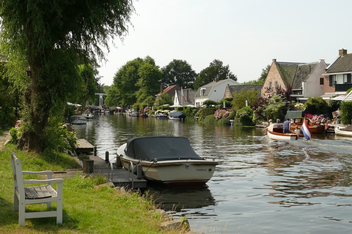 Sloep op kanaal met op achtergrond bootje met familie en huizen 
