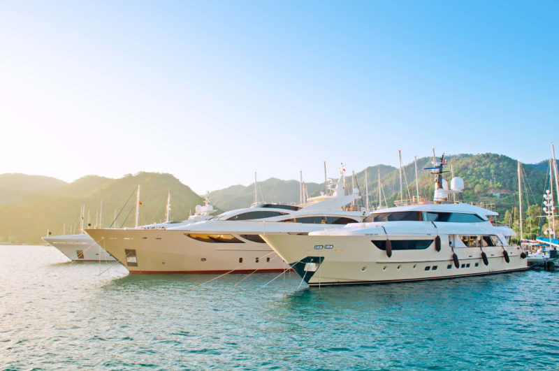 Two Yachts on open water, green mountains and blue skies to the background