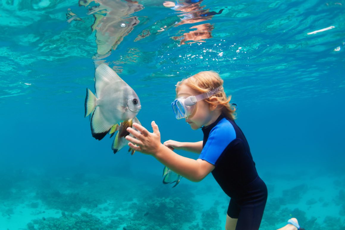 Happy family - active kid in snorkeling mask dive underwater, see tropical fish Platax ( Batfish ) in coral reef sea pool. Travel adventure, swimming activity on summer beach vacation with child.