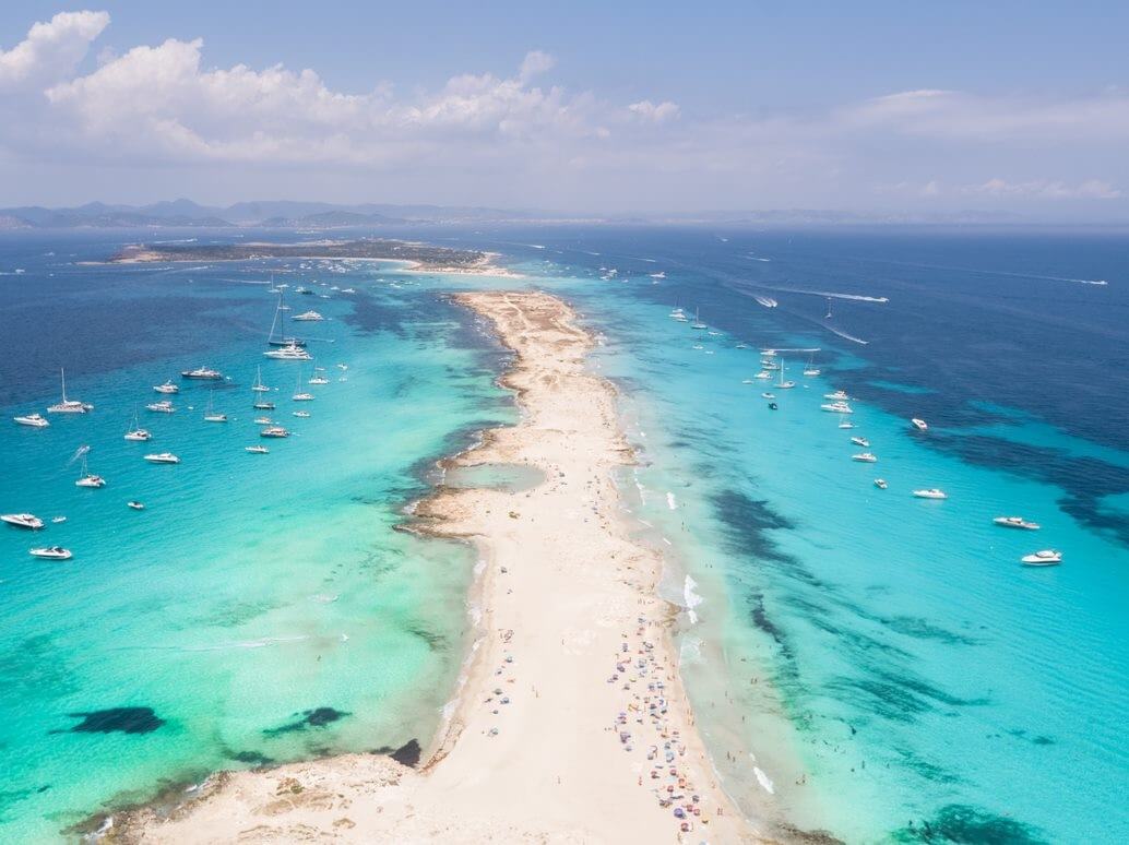 aerial view of a small strip of sand and yachts anchored in bright blue water in the Balearic Islands
