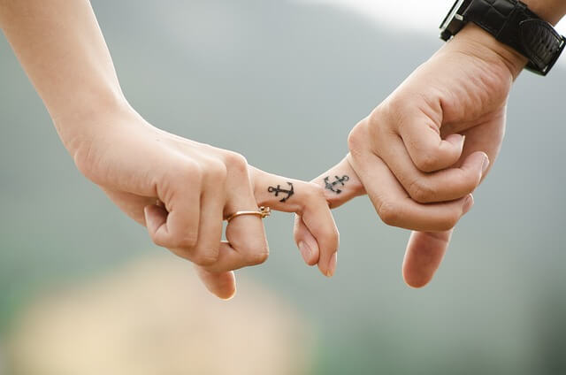 hands holding with matching anchor tattoo on pointer finger