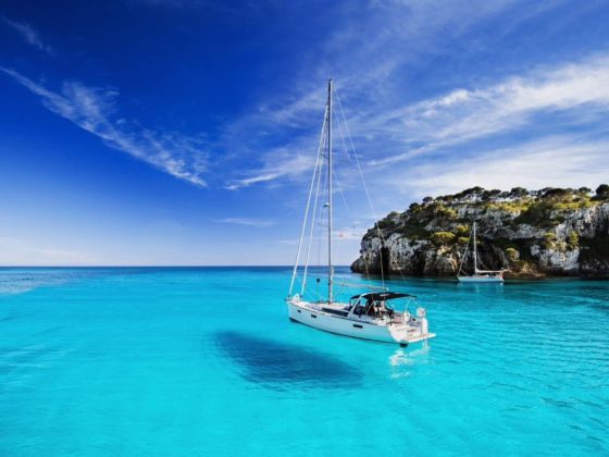 boat floating in turquoise water with rocky cliff in the background