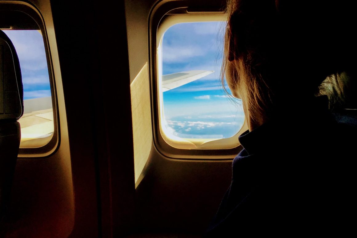A person looking out of an airplane window at the ocean during a bleisure trip