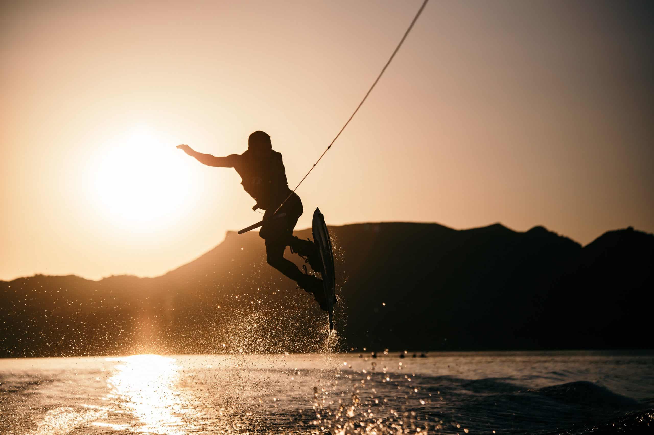 Un homme pratiquant une activité en bateau : le wakeboard, sur fond de coucher de soleil.