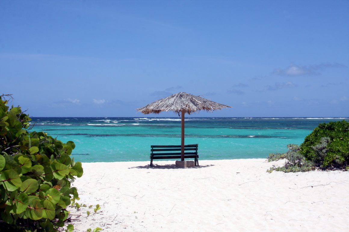 Plage de sable blanc à Anegada avec parasol en chaume face à la mer turquoise