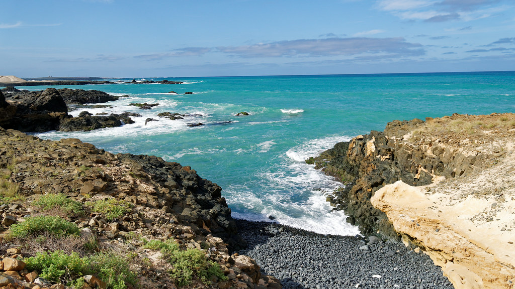 Côte rocheuse et mer turquoise au Cap-Vert, avec plage de galets noirs.