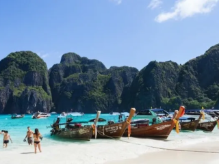 Long-tail boats et baigneurs sur une plage de sable blanc en Thaïlande, entourée de falaises
