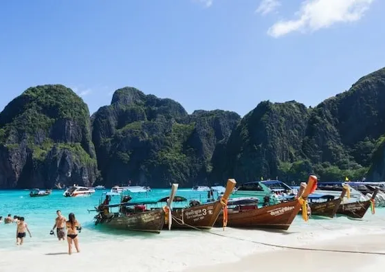 Long-tail boats et baigneurs sur une plage de sable blanc en Thaïlande, entourée de falaises