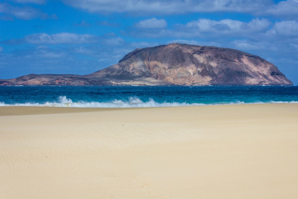 Plage de Las Conchas avec vaste sable clair et îlot au loin.