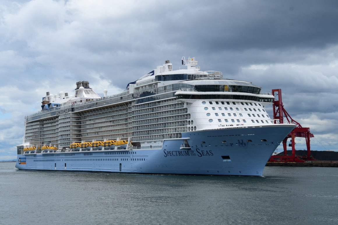 Grand navire de croisière Spectrum of the Seas amarré au port, sous un ciel nuageux, avec des grues rouges en arrière-plan.