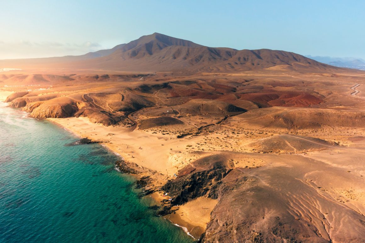Plage volcanique à Lanzarote avec mer turquoise et reliefs arides.