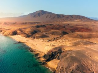 Plage volcanique à Lanzarote avec mer turquoise et reliefs arides.