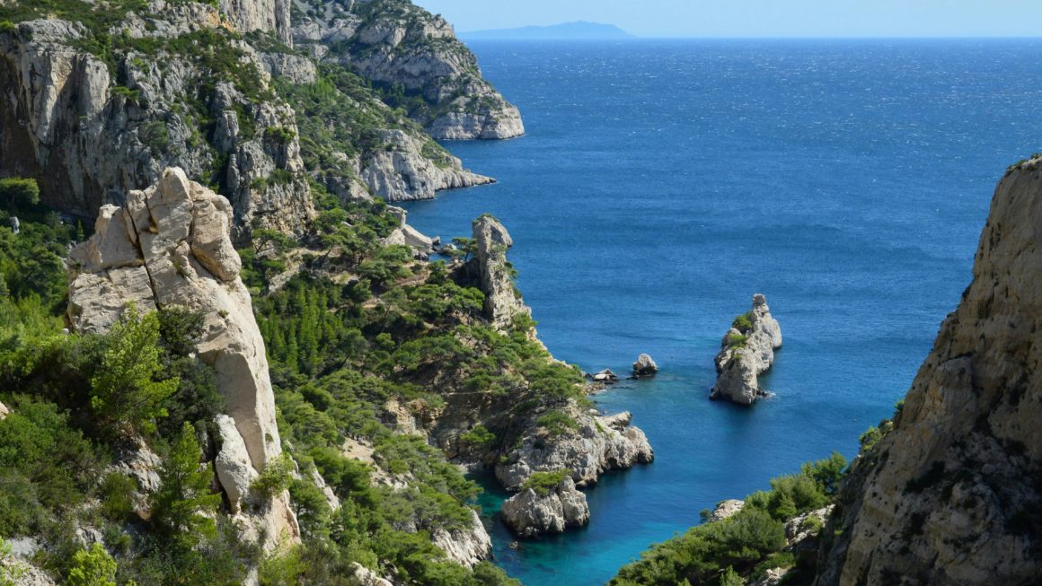 Vue plongeante sur les falaises calcaires et l'eau bleu profond d'une calanque à Marseille.
