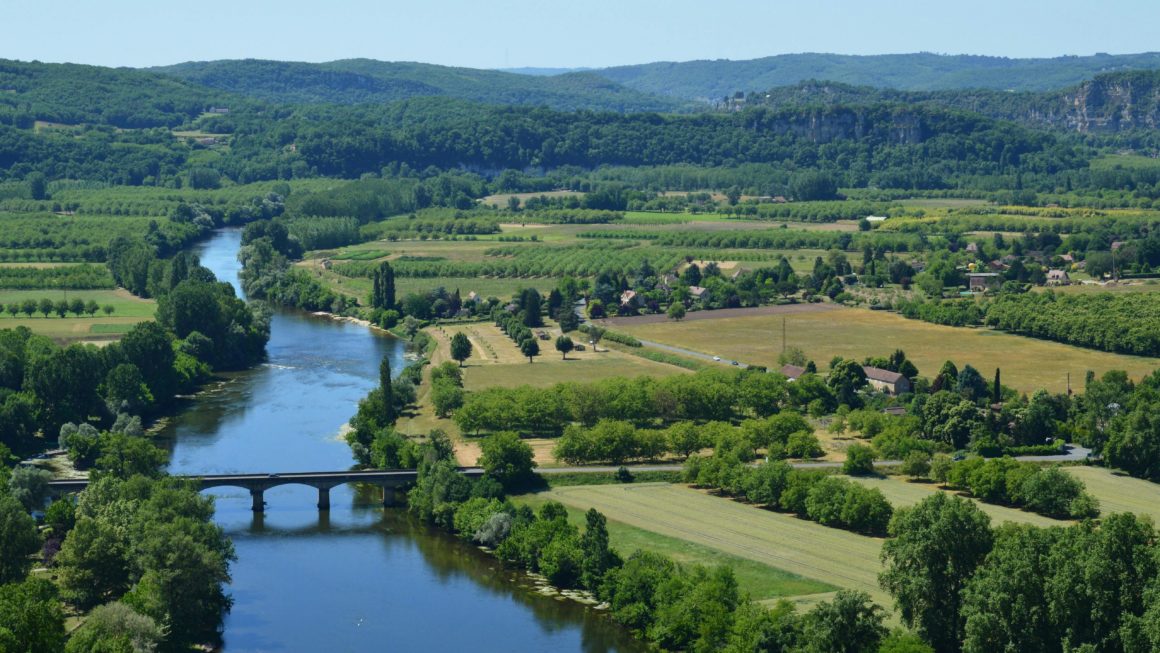 Vue panoramique verdoyante d'un fleuve serpentant à travers la campagne française sous un ciel bleu.