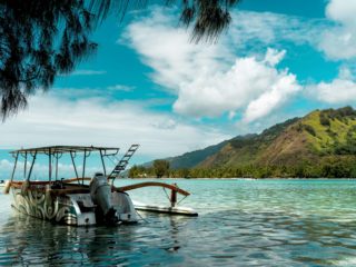 Bateau au mouillage dans un lagon turquoise face à une montagne verdoyante.