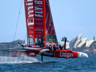 Catamaran de compétition Emirates Team New Zealand volant sur ses foils devant l'Opéra de Sydney.